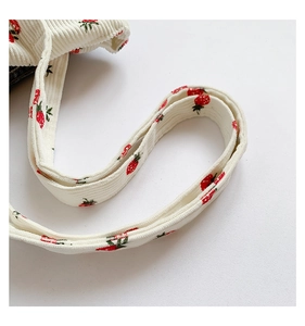 Detailed close-up of cream corduroy shoulder strap with red strawberry prints on the tote bag