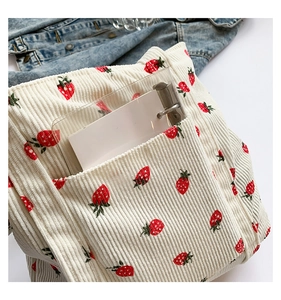 Detail of white corduroy tote bag featuring red strawberry prints and side pocket