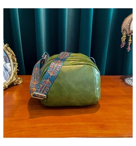 Olivgrüne PU-Muscheltasche mit gewebtem Boho-Gurt auf einem rustikalen Holztisch