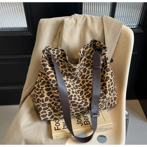 Close-up of leopard print canvas tote bag featuring brown leather strap on a beige chair