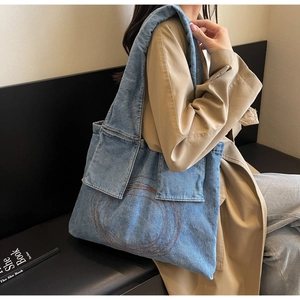 Detail of blue denim tote bag with circular embroidery worn on model's shoulder