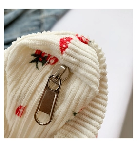 Detailed close-up of a silver zipper on a white corduroy tote bag with strawberry prints