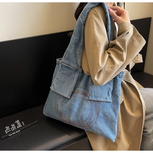 Detail of blue denim tote bag featuring dual front pockets and spiral embroidery detail