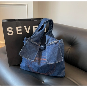 Close-up of dark blue denim tote bag with orange contrast stitching and embroidery details
