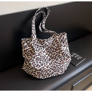 Detailed close-up of large leopard print tote bag placed on a black leather bench