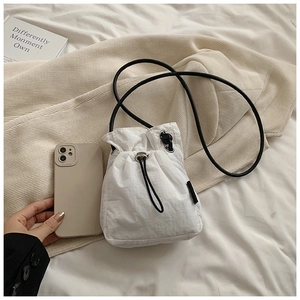 Close-up of white mini nylon drawstring bag with black strap next to a smartphone