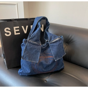Close-up of dark blue denim tote bag with orange circular stitching on a leather sofa