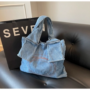 Detailed view of blue denim tote bag featuring circular embroidery and two flap pockets