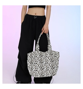 Detail of a large leopard print canvas tote bag carried by a model against a soft backdrop