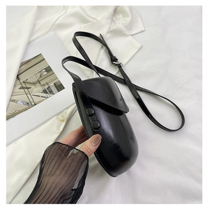 Close-up of glossy black saddle bag with silver round buckle and thin shoulder strap