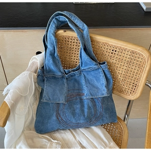 Close-up of blue denim tote bag with red circular embroidery on a wicker chair background