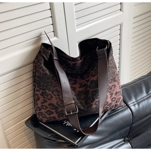 Detail of leopard print canvas tote bag featuring wide brown leather strap and metal buckle