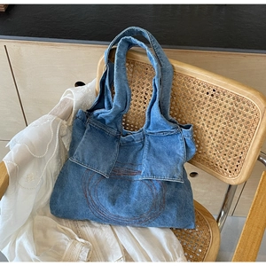 Detail of blue denim tote bag with circular embroidery placed on a wicker chair