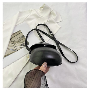 Close-up of a black glossy semi-circular saddle bag held by hand in a minimalist setting
