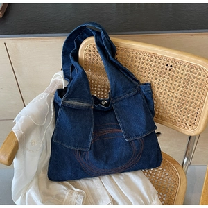 Detail of dark blue denim tote bag with decorative orange stitching and functional pockets