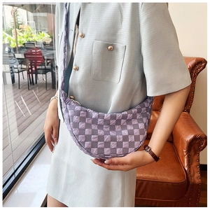 Dettaglio di una borsa a mezzaluna a scacchi viola indossata su un abito azzurro