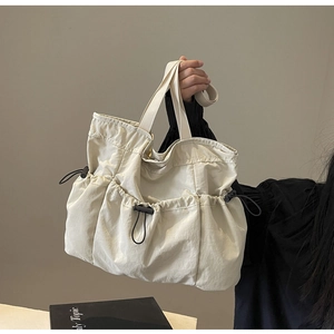 Detail of off-white nylon tote bag showing three pockets with black adjustable drawstrings
