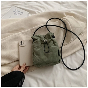 Green mini nylon drawstring bag with adjustable strap shown next to a mobile phone