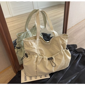 Detail of a pleated nylon tote bag featuring functional drawstring pockets and dual handles