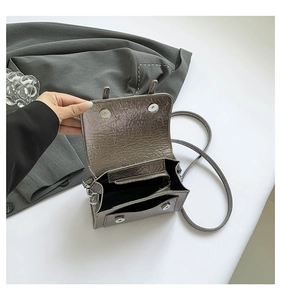 Internal view of silver metallic messenger bag showing dual magnetic buckles and zip pocket