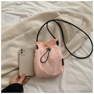Detail of a mini pink nylon drawstring bucket bag next to a mobile phone for size comparison