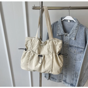 Detail of off-white canvas tote bag with black drawstring ruching and wide shoulder strap