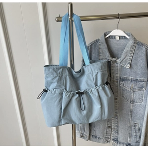 Close-up of light blue pleated tote bag with drawstring pockets and blue woven handles
