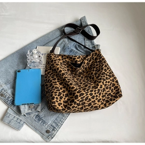 Flat lay of large leopard print canvas hobo bag with leather strap on denim jacket