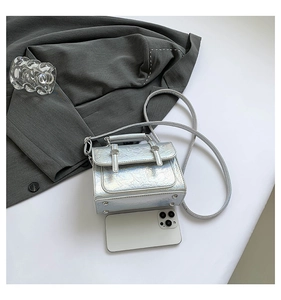 Mini silver holographic messenger bag size comparison with a mobile phone on a suit jacket