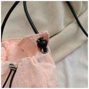 Detail of pink nylon drawstring bag showing grid texture, silver eyelet and black toggle