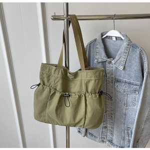 Detail of olive green canvas tote bag with three drawstring pockets and brown web handles