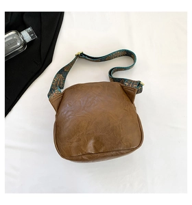 Braune Vintage-Muschel-Umhängetasche mit blauem Ethno-Riemen auf weißem Stoffhintergrund