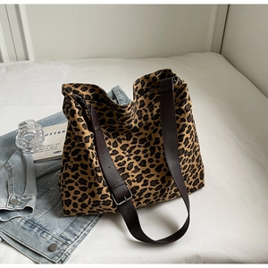 Detail of leopard print canvas tote bag with brown leather straps on a white bed