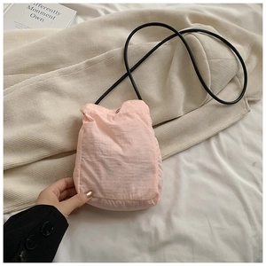 Detail of pink mini drawstring nylon crossbody bag with textured fabric and black cord strap