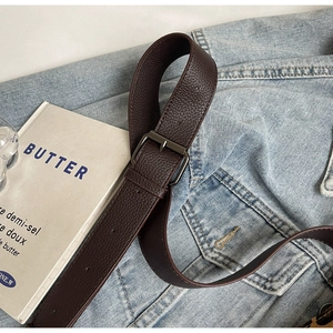 Detailed close-up of dark brown pebbled leather belt with metal buckle on denim jacket