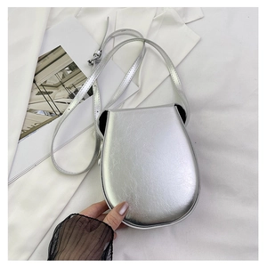 Detail of silver metallic saddle crossbody bag with rounded design and thin shoulder strap