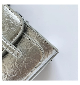 Detail of silver metallic messenger bag featuring cracked texture and fine grey edge stitching