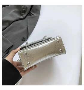 Detail view of the silver metallic bag base featuring four protective metal rivets and texture