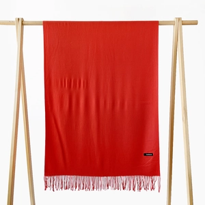 Detail of red cashmere scarf with fine tassels hanging on a wooden rack against white