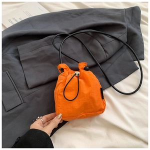 Top view of bright orange nylon drawstring mini bag on a casual lifestyle background