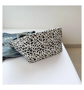 Leopard print tote bag displayed with denim jacket and glass on a white platform