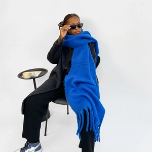 Detail of royal blue thick mohair scarf with long tassels worn by a model in studio