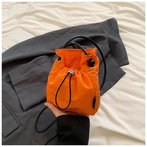 Detail of bright orange drawstring bucket bag in textured nylon fabric with black side label