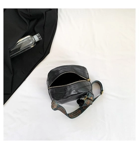 Draufsicht einer schwarzen PU-Ledertasche mit buntem gewebtem Gurt auf weißem Stoff