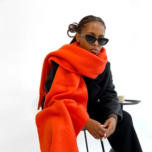 Detailed close-up of orange mohair scarf with thick knit texture and long tassel trim