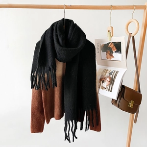Detail of long thick black mohair scarf with tassels hanging on a wooden hanger