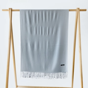 Close-up of a light blue cashmere scarf showing fringe and black label on a wooden rack