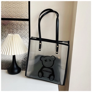 Detail view of transparent PVC tote bag with black bear print and gold rivet accents