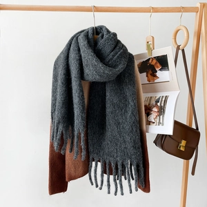 Detail of dark grey thick knit scarf with long tassels draped on a brown sweater