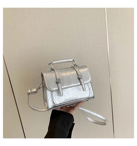 Detail of silver metallic messenger bag with wrinkled texture and top handle